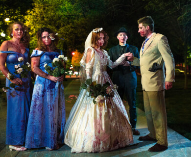 People in formal attire, including a bride and bridesmaids, with fake blood in a park at night.