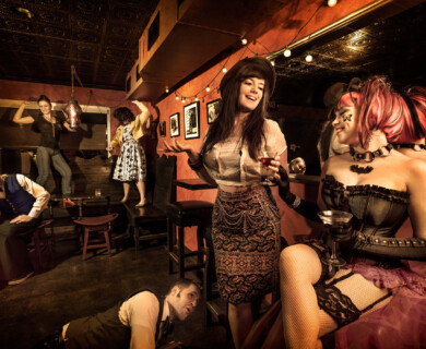 Bar scene with people in eclectic costumes dancing, posing and enjoying drinks amidst vintage decor.