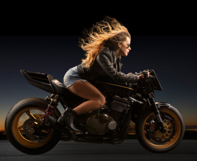 Person on a sleek motorcycle with golden wheels, hair blowing, dark blurred background.