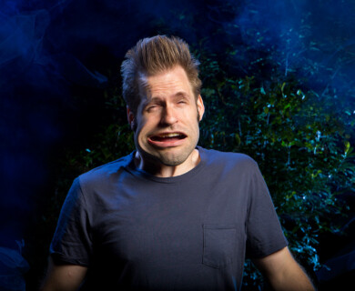 Person outdoors at night with distorted expression, dark background, bluish light, green foliage.