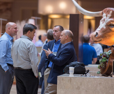 A group of four men are engaged in conversation in a large indoor space, possibly a conference. To the right, there is a decorative sculpture of a longhorn steer and a sign that reads "Welcome Hygienix 2017." Four men converse in a large indoor space near a steer sculpture, with "Welcome Hygienix 2017" sign.