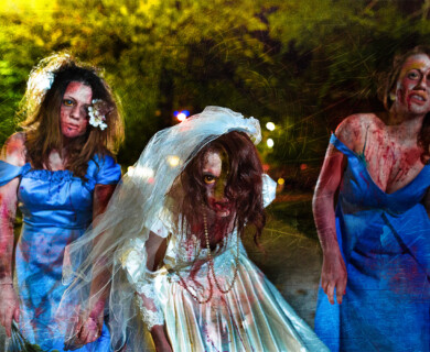 Three people in zombie bride and bridesmaid costumes posing outdoors at night with spooky backdrop.