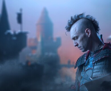 A person in armor is standing in front of a blurred medieval castle. The figure has a mohawk hairstyle and appears to be looking downwards, with a somber expression. The scene is set against a misty, atmospheric background. Person in armor with mohawk stands before a blurred medieval castle in a misty setting.