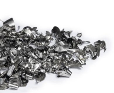 A pile of metallic shavings and curls is scattered on a white surface, consisting of shiny, irregular pieces with sharp edges and varied shapes. Metallic shavings and curls scattered on a white surface with varied shapes and sharp edges.