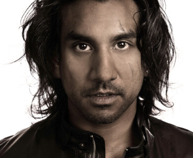 A person with long dark hair is wearing a leather jacket. The image is in black and white, highlighting facial features and textures. Person with long dark hair in leather jacket, black and white photo emphasizing textures.