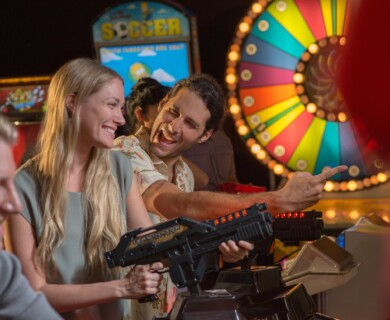 Arcade scene with people playing shooting games, colorful wheel and machines in background.
