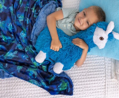 Child in bed with blue plush llama, sea turtle blanket, and blue pillow.