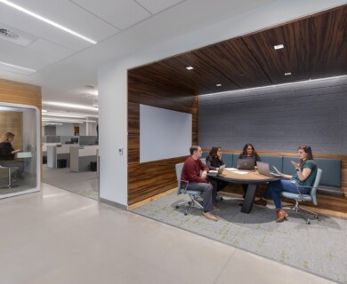 Modern office with meeting area, four people using laptops, soundproof booth, and open workstations.
