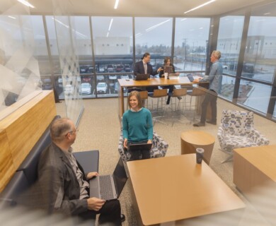 Modern office with people working, large windows, contemporary furniture, open, bright layout.