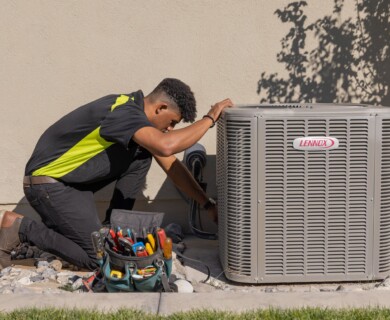 Person kneels beside Lennox AC unit, performing maintenance with tools nearby on rocks.