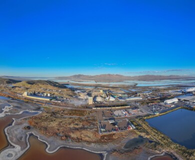 Aerial view of an industrial complex surrounded by water bodies and salt flats, with hills in the background under a clear blue sky. Aerial view of industrial complex with salt flats and water, hills in the background, clear sky.